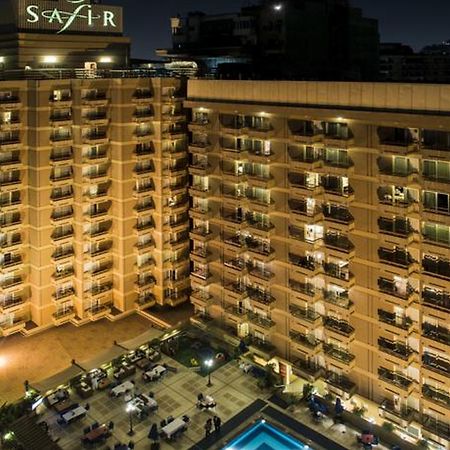 Safir Hotel Cairo Giza Bagian luar foto The photo shows a multi-story hotel building at night. The building is illuminated, showcasing multiple balconies along its facade. In front of the hotel, there is an outdoor area with seating arranged around a pool, which is also lit up. The hotel's