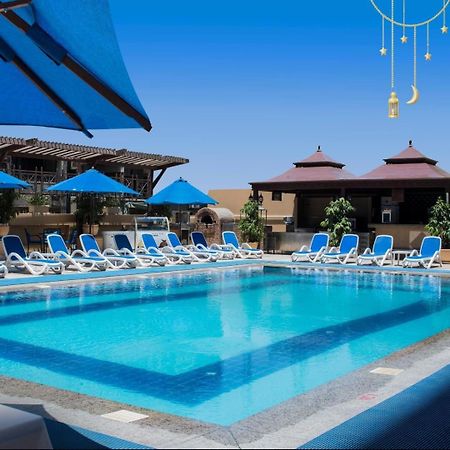 Safir Hotel Cairo Giza Bagian luar foto The photo showcases a bright, inviting swimming pool surrounded by lounging chairs. The pool is set in a sunny outdoor area, with clear blue water reflecting the sky. There are several blue umbrellas providing shade over the lounge chairs, which are 