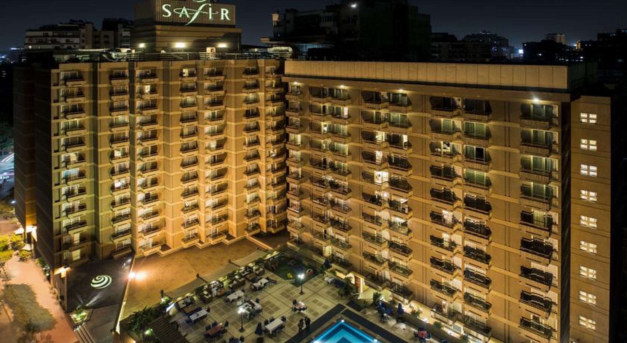 Safir Hotel Cairo Giza Bagian luar foto The photo shows a multi-story hotel building at night. The building is illuminated, showcasing multiple balconies along its facade. In front of the hotel, there is an outdoor area with seating arranged around a pool, which is also lit up. The hotel's