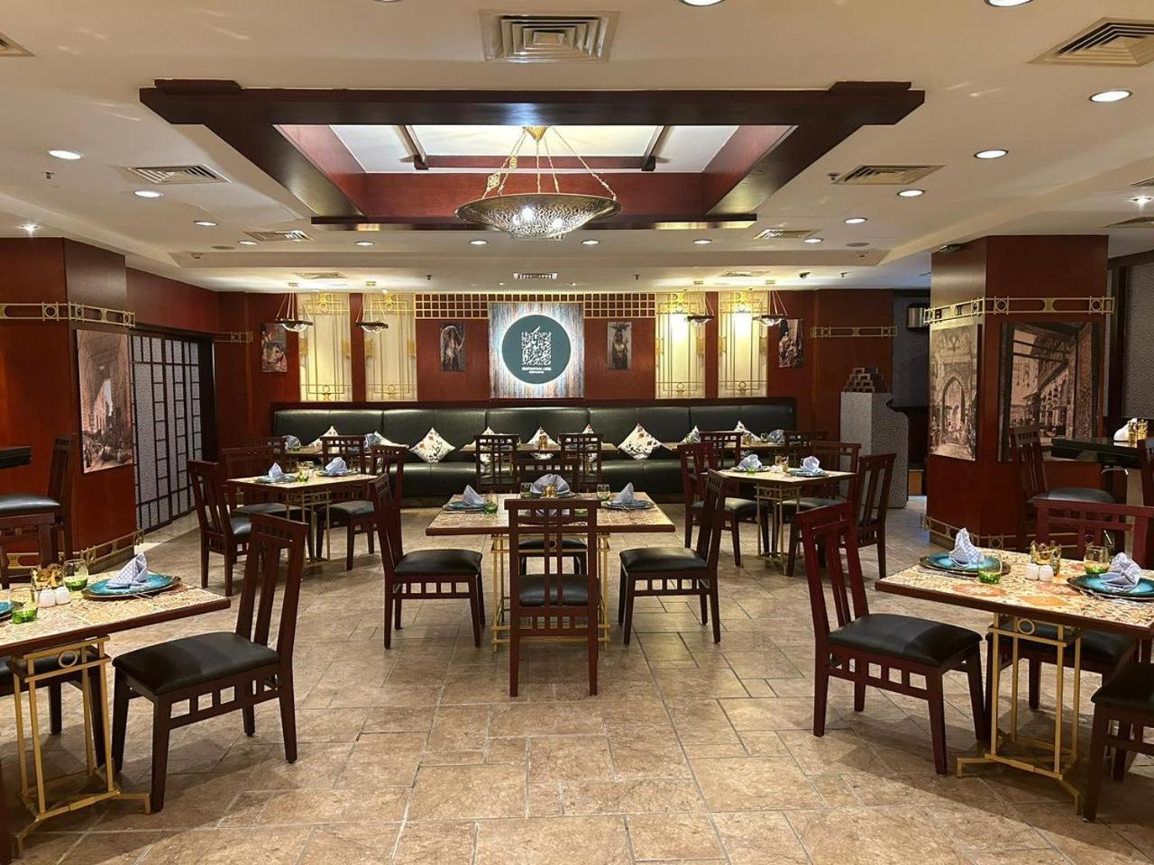 Safir Hotel Cairo Giza Bagian luar foto The photo shows the interior of a restaurant. The space features a combination of warm wood tones and elegant decorations. There are several dining tables arranged throughout, each set with plates, cutlery, and decorative napkins. The walls are adorn