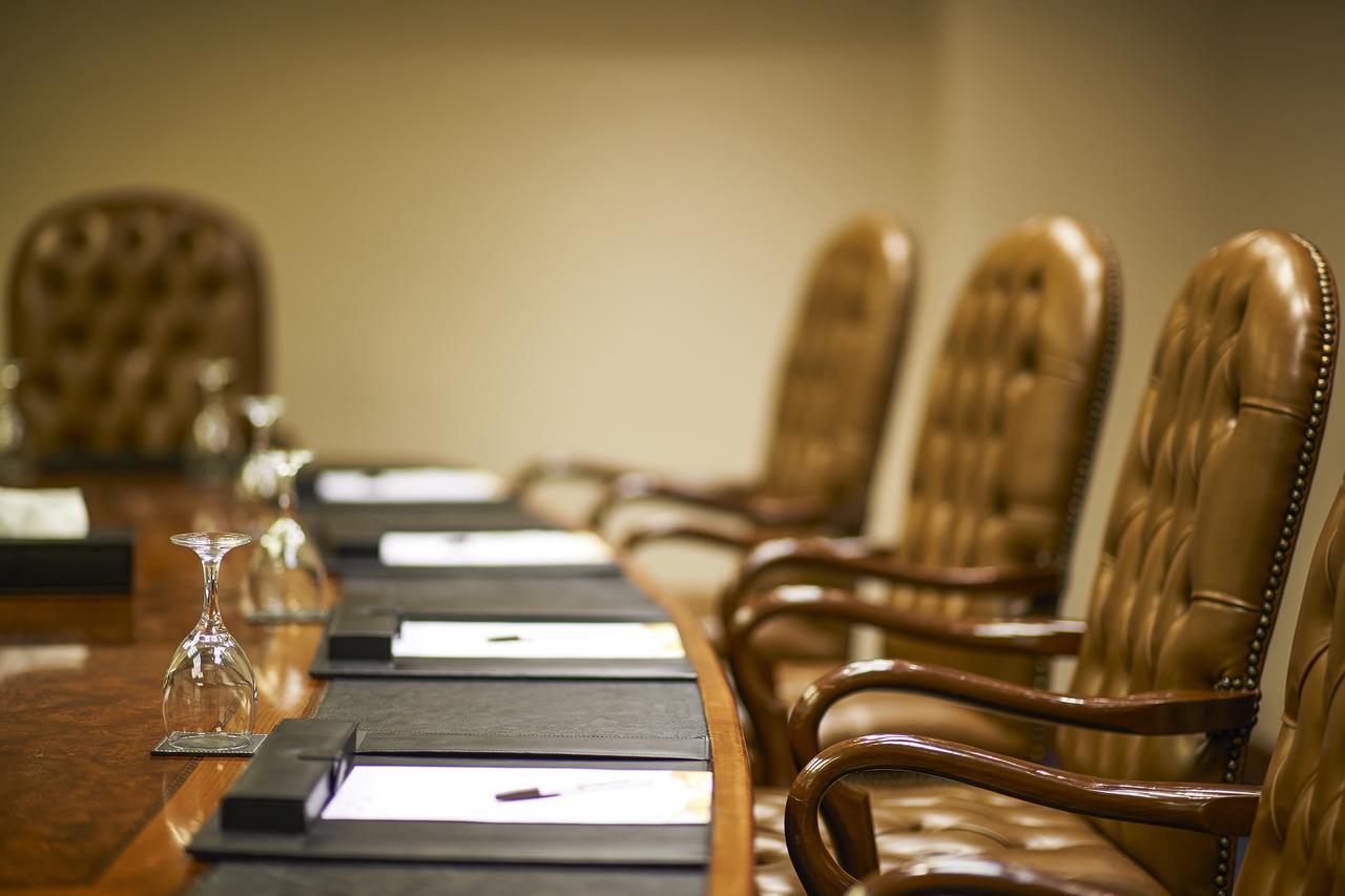 Safir Hotel Cairo Giza Bagian luar foto The photo shows a conference room setting with a long wooden table and several high-backed chairs. The chairs appear to be upholstered in a brown leather material. Each place at the table has a black folder or pad, and there are also glass water gobl