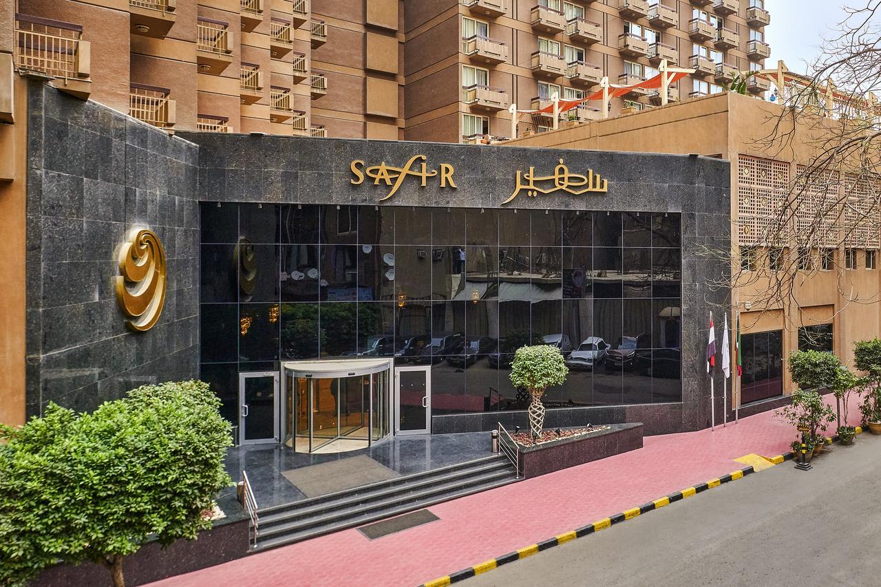 Safir Hotel Cairo Giza Bagian luar foto The photo depicts the entrance of a modern building, which appears to be a hotel or a commercial establishment. The facade features a large glass front with reflective surfaces. Above the entrance, there is a prominent sign displaying the name of the