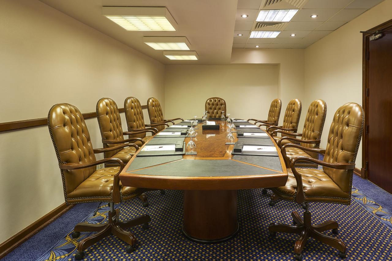 Safir Hotel Cairo Giza Bagian luar foto The photo shows a conference room with a large oval table surrounded by several brown leather chairs. There are eight chairs in total, each with a high back and wheels. The table has some notepads and glasses of water set up on it. The room has neutr