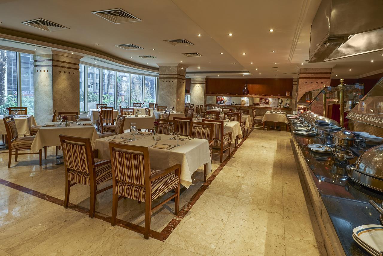 Safir Hotel Cairo Giza Bagian luar foto The photo shows the interior of a restaurant. It features a spacious dining area with several tables laid out with white tablecloths. The tables are accompanied by wooden chairs that have striped patterns. The restaurant is well-lit with soft lightin