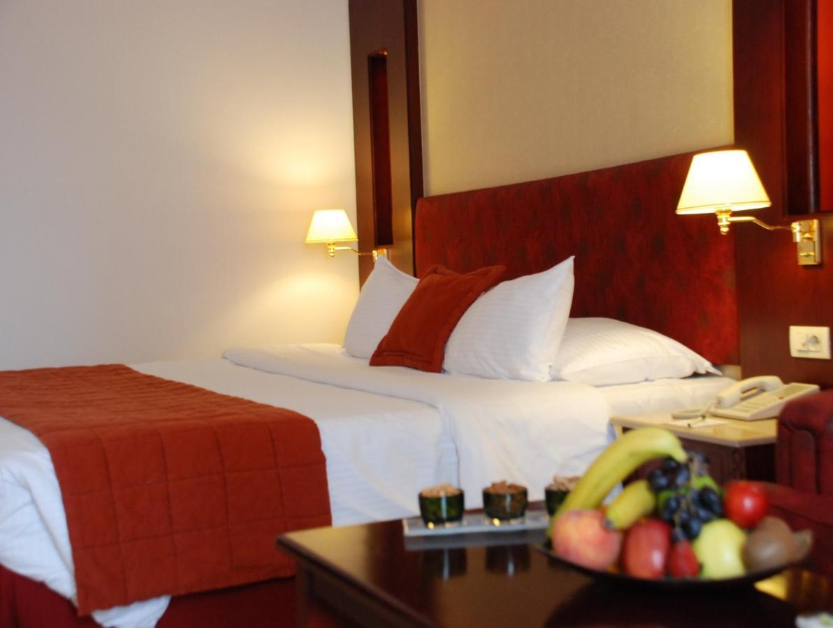Safir Hotel Cairo Giza Ruang foto The photo shows the interior of a hotel room featuring two beds with white bedding and an orange throw blanket. There are decorative pillows on the beds. The walls are designed in warm tones, and there are two bedside lamps providing soft illuminatio